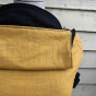 Close up of an Integra eco-friendly gold linen baby carrier in front of a wooden fence