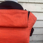 Close up of an Integra eco-friendly rust linen baby carrier in front of a wooden fence