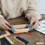 Close up of some hands stacking the Kapla natural and blue wooden toy blocks into a square shape on a wooden table