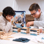 Close up of two boys laying down building towers with the Kapla plastic-free Waldorf toy blocks on a white carpet