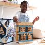 Girl sat on the floor stacking wooden Kapla toy blocks into the shape of a building