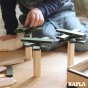 Close up of child's hand stacking the green Kapla wooden building shapes into towers on a beige floor