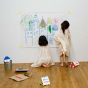 Two girls drawing with the Kitpas crayons on a large sheet of paper, taped to a wall