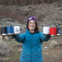 An adult happily holding 6 Klean Kanteen Camping mugs in their hands. On the left is a black, blue and a white etched mountain mug, and on the right is a white, red and black etched mountain mug