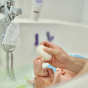 A newborns foot is being washed by an adult using a Kokoso Konjac Natural Baby Konjac Bath Sponge. The bath is white and out of focus, just the hand of the adult, newborn foot and sponge are in focus.