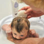 Newborn baby in bubbly bath being supported by adult arm. Baby is being gently washed with Kokoso Natural Baby Konjac Bath Sponge