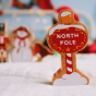Lanka kade plastic free wooden north pole toy sign on a white sheet in front of some lanka kade festive christmas toy figures