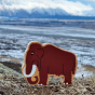 Close up of the Lanka Kade brown mammoth toy figure stood on some grass in front of a snowy mountain