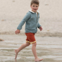 Boy walking on some wet sand wearing red shorts and a blue sherpa collar LGR jacket