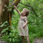 Young girl reaching up to a tree, wearing the LGR short sleeve organic cotton dress in the rainbow stripe and garden print