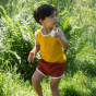 Child wearing a yellow gold coloured vest with rust coloured shorts 