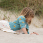 Young girl laying on some sand in a white dress and blue knitted LGR cardigan