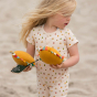 Close up of girl holding some yellow soft toys, wearing the LGR shortie romper suit in the garden print