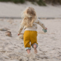 Young girl running on a beach wearing the LGR yellow reversible kids trousers