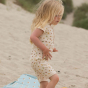 Girl walking on some sand wearing the LGR garden print short romper suit