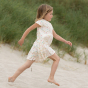 Girl running on the beach wearing the LGR white organic cotton rainbow spots dress