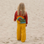 Girl stood backwards on some sand wearing yellow trousers and a red knitted cardigan with a rainbow design on the back