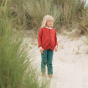 Young girl stood on a beach wearing an LGR red organic cotton knitted cardigan