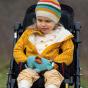Child wearing the Little Green Radicals Adaptive Easy Feeding Sunshine & Rainbows T-Shirt with a yellow sherpa jacket and rainbow striped knitted hat