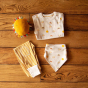 A flatlay featuring the Little green Radicals Adaptive Extra Long Gold Striped Joggers folded along side a sunshine and rainbows print top and a matching dribble bib and sunshine shaped soft toy 