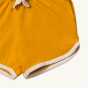 A closer view of the cream piping on the Gold Run Around Shorts. Made from GOTS Organic Cotton, these shorts are a rich gold colour, with off white piping on the legs, drawstring and side pockets for treasures