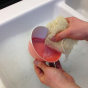 person washing a small pink and white bowl with a LoofCo Loofah Washing-Up Pad