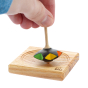 Close up of a hand holding the Mader plastic-free wooden superstar spinning top on a mini spinning plate on a white background