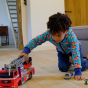 A young child plays indoors with a fire engine wearing the Maxomorra Fire Truck Reversible Zip Hoodie.