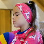 Maxomorra- A young girl plays with a toy whilst wearing a unicorn motif headband. Headband side detail.