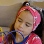 Maxomorra- A young girl plays with a toy whilst wearing a unicorn motif headband. Headband front detail.