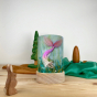Toverlux Light Wishes Base and Silhouette in Mermaid. A beautiful felt illustration on a mermaid finding a pearl. The Light Wish is set on a wooden table with a wooden rabbit in front, green and brown fabric behind with wooden trees