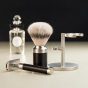 Muhle stainless steel rocca shaving set laid out on a black and white background in front of an aftershave bottle