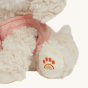 The Olli Ella Dinkum Dog "Cookie" has an embroidered paw print on its paw, in the shape of a rainbow.