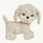 The Olli Ella Dinkum Dog "Cookie" is a dog shaped stuffed toy with soft cream coloured fur, a cute round face, long ears, and a little pink tongue sticking out.