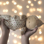 Olli Ella Dozy Dinkum Doll Custard in cream outfit with red tulip flower patterns being held by child, with fairy lights in the back ground