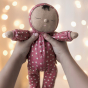 Olli Ella Dozy Dinkum Doll Pie in red outfit with white tulip flower print held by child, with fairy lights in back ground