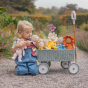Olli Ella Dinky Dinkum Blossom Buds - Sunny Sunflower  is sat in an Ollie Ella wagon surrounded by the rest of the blossom bud range with a child holding two  dolls 