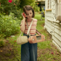 Girl holding something to her ear wearing the Olli ella mini chari bag in a green garden
