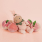 Olli ella pink peach dinky doll toy sat next to some peaches on a pink background