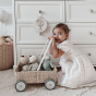 Young girl crouched down next to the Olli Ella rattan Wamble Walker push-along toy basket, in front of some white drawers