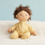 Olli Ella dinkum doll sat on a white blanket wearing the goldie striped doll pyjamas
