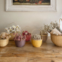 Olli Ella handmade rattan blossom baskets lined up on a wooden floor, filled with different coloured flowers