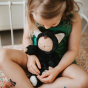Olli Ella Cozy Dinkums - Black Cat Nox rests on a child's lap, the young girl cuddles the toy.