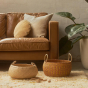 Olli Ella woven seagrass display bowls on a fluffy carpet in front of a brown sofa and a large potted plant