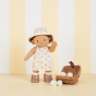 Olli Ella dinkum doll stood on a cream background next to a wooden basket wearing the una rainbow dress set 