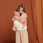 Girl cuddling a dinkum doll toy in her Olli Ella soft rainbow baby carrier accessory in front of a brown sheet background