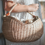 Close up of person holding the Olli Ella woven rattan half moon basket under their forearm