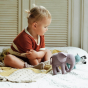 A toddler playing with the Olli Ella Holdie Folk Safari Animals, sat on a bed on a knitted blanket, wooden shutters in the background