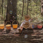 Young child sat on a log with different coloured Olli Ella blossom rattan carry baskets beside them