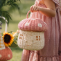 Picture of a child holding the Olli Ella Mushroom Rattan basket with a spotted pink mushroom cap, a door, and windows.